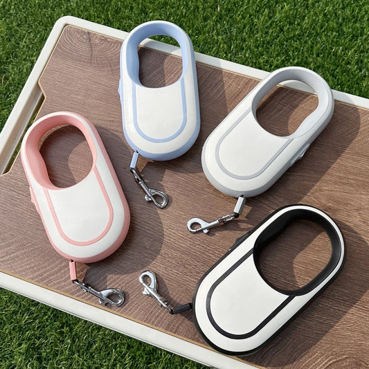retractable dog leash shown in 4 available colors placed on cutting board above grass