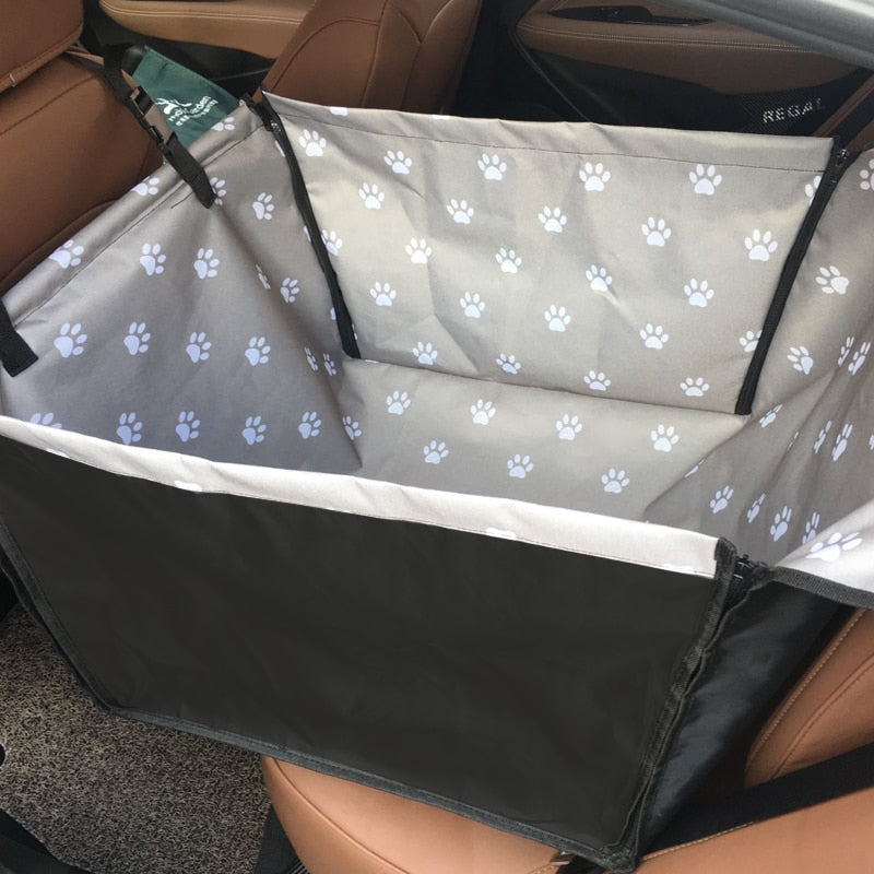 Single seat automotive pet carrier in gray with white paw prints, shown fully zipped in the back seat.