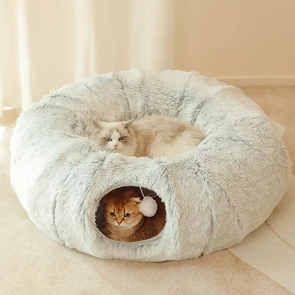 A semi-enclosed donut shaped plush cat bed and two cats.