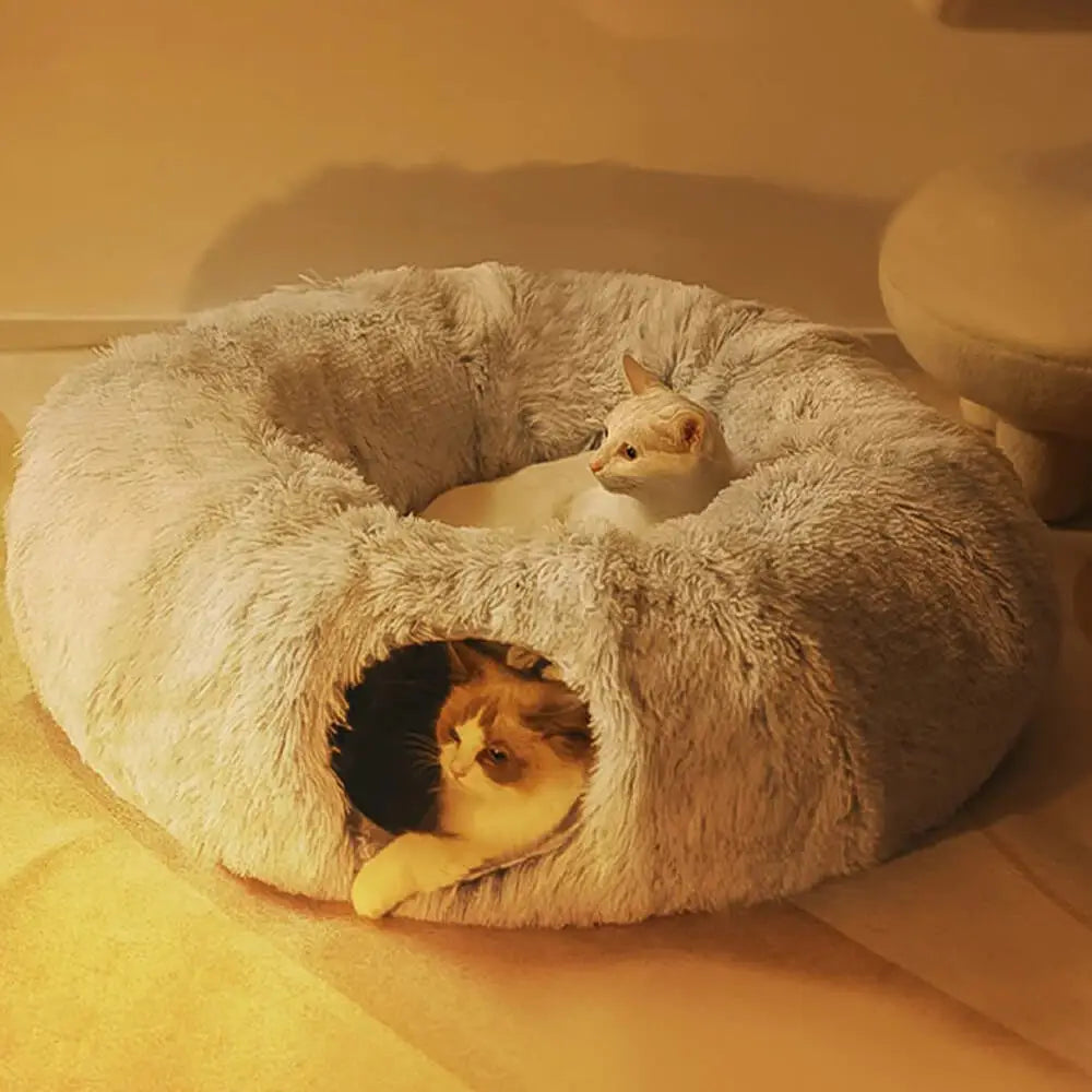 A semi-enclosed donut shaped plush cat bed and two cats.